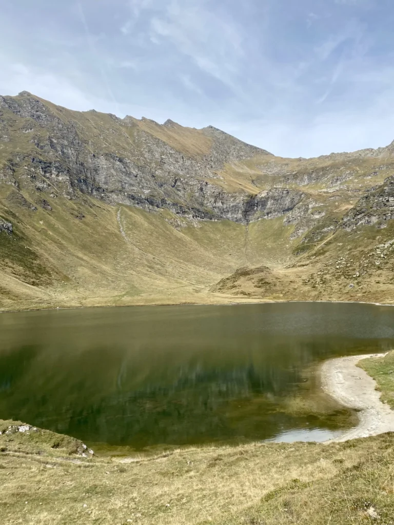 Piccolo lago alpino di Tom, circondato da pendii erbosi e montagne rocciose nella Val Piora, Ticino