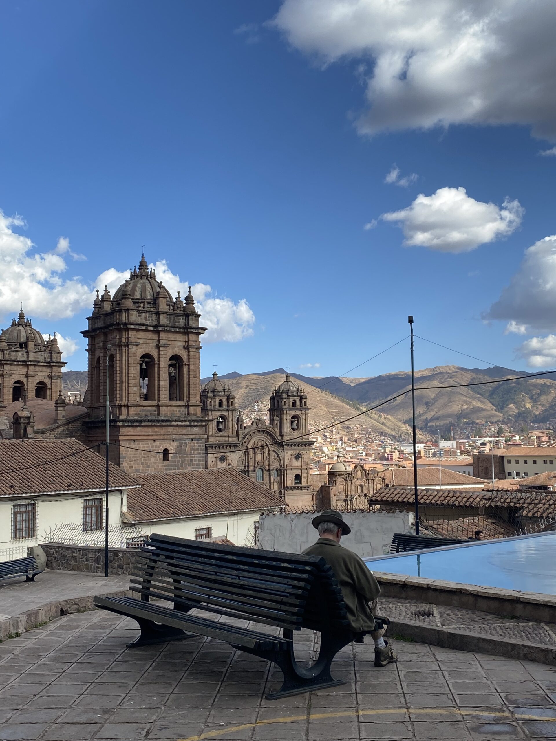 Uomo seduto su una panchina con vista sulla Cattedrale e la città di Cusco