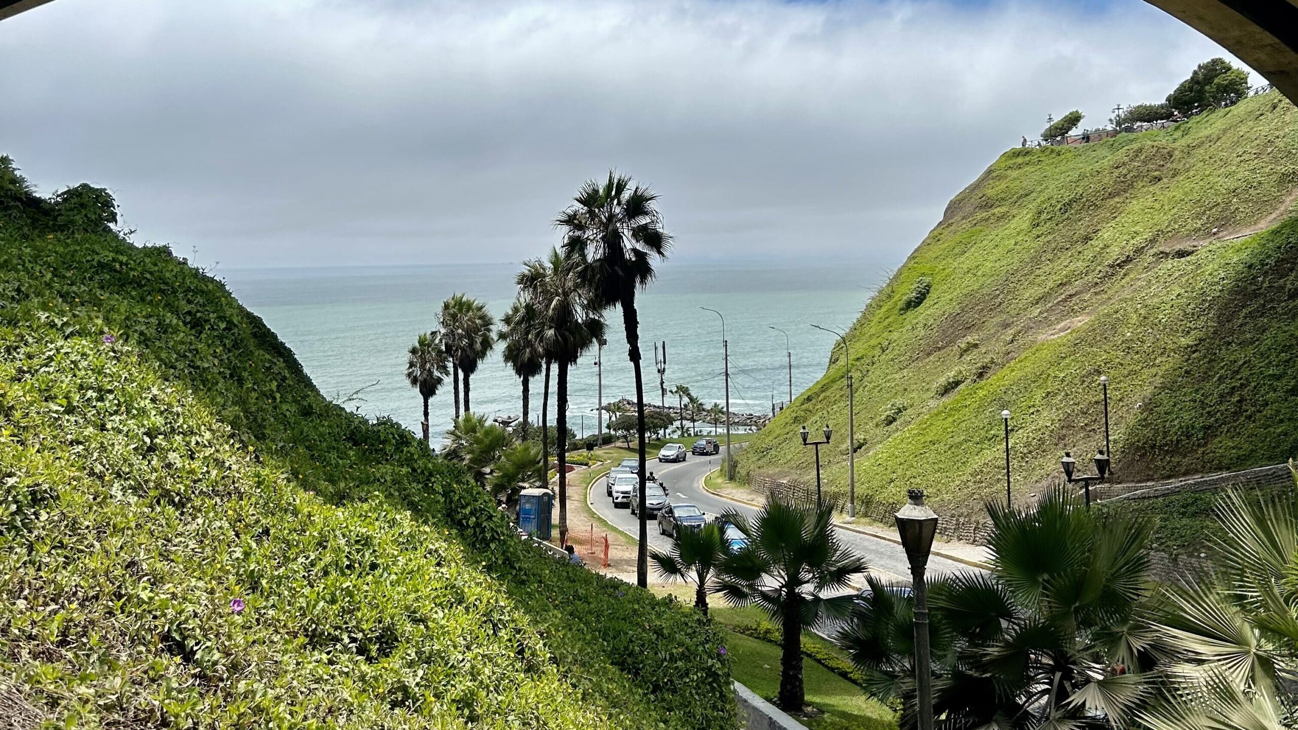 Vista dell’Oceano Pacifico dal ponte Villena Rey a Miraflores, Lima, con palme e strada costiera in primo piano.