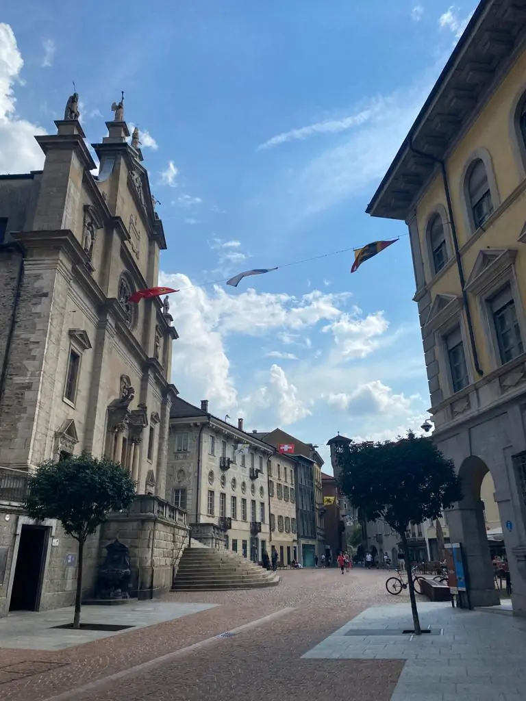 Centro storico di Bellinzona con la Collegiata dei Santi Pietro e Stefano, bandiere ticinesi e cielo estivo